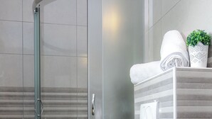 Un bany modern amb dutxa de vidre, vàter blanc i una petita planta en maceta a la superfície del lavabo.