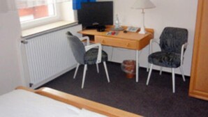 Una habitación de hotel con cama, escritorio con computadora, silla, televisor y ventana con cortinas.