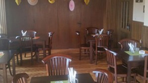 Un comedor con mesas y sillas de madera, una puerta de madera y un techo con lámparas colgantes.