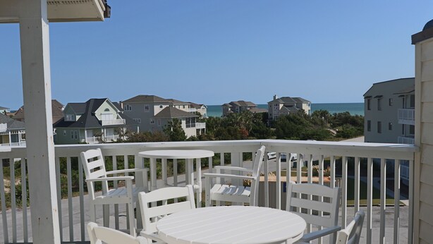 A balcony with white furniture, a view of houses, and the ocean.