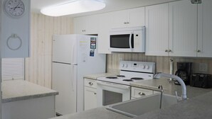 A kitchen with white cabinets, a microwave, a refrigerator, a stove, and a sink.