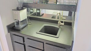 A kitchen area with a coffee maker, a sink, and a mirror reflecting the room.