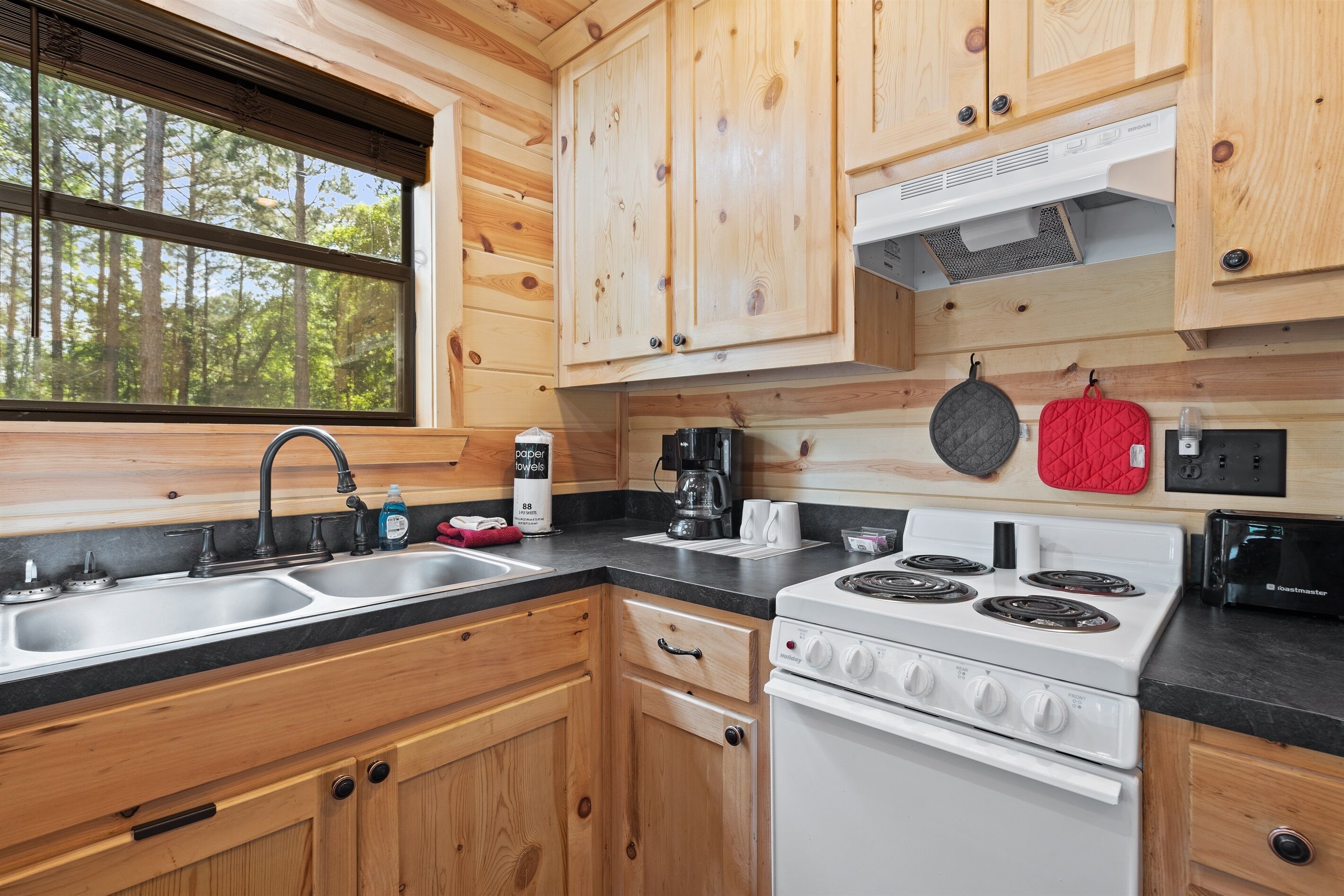 Una cucina con mobili in legno, un fornello, un lavello e una finestra con vista su una foresta.