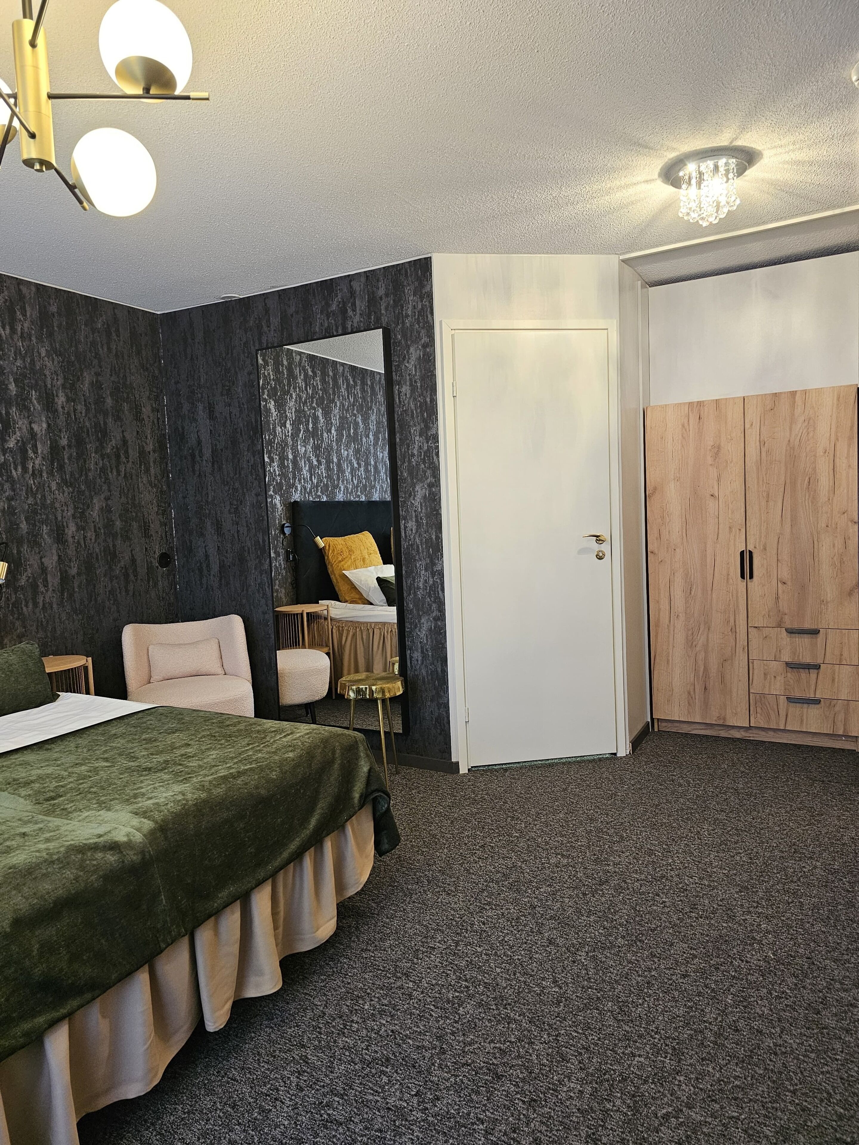Un dormitorio con cama, una silla, una mesita, un espejo, un armario y una puerta.