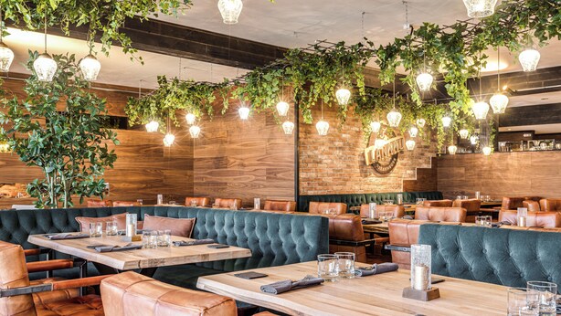 A restaurant with wooden walls, green upholstered booths, and hanging light fixtures. - Samantta Hotel & Restaurant (Oulu)