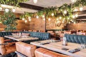 Un restaurante con paredes de madera, asientos tapizados en verde y lámparas colgantes.
