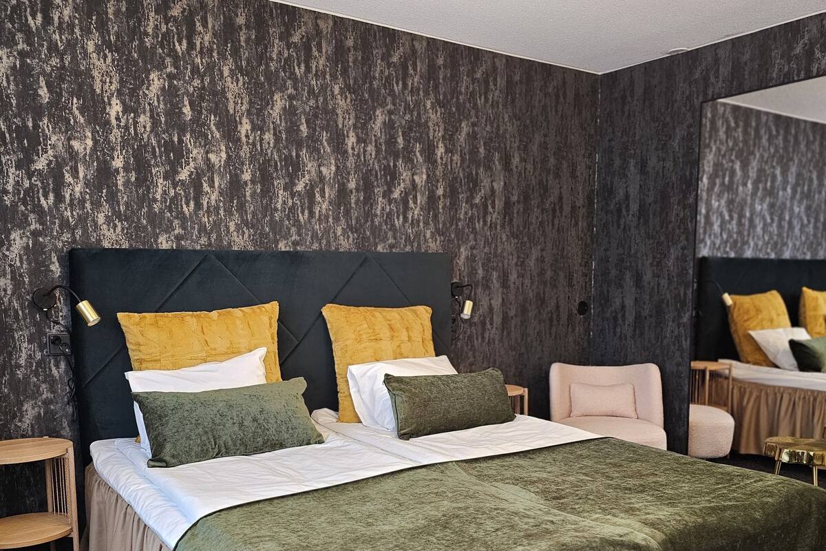 Ein modernes Schlafzimmer mit einem großen Bett, einem Kopfteil, Nachttischen, einem Sessel und einem Spiegel.