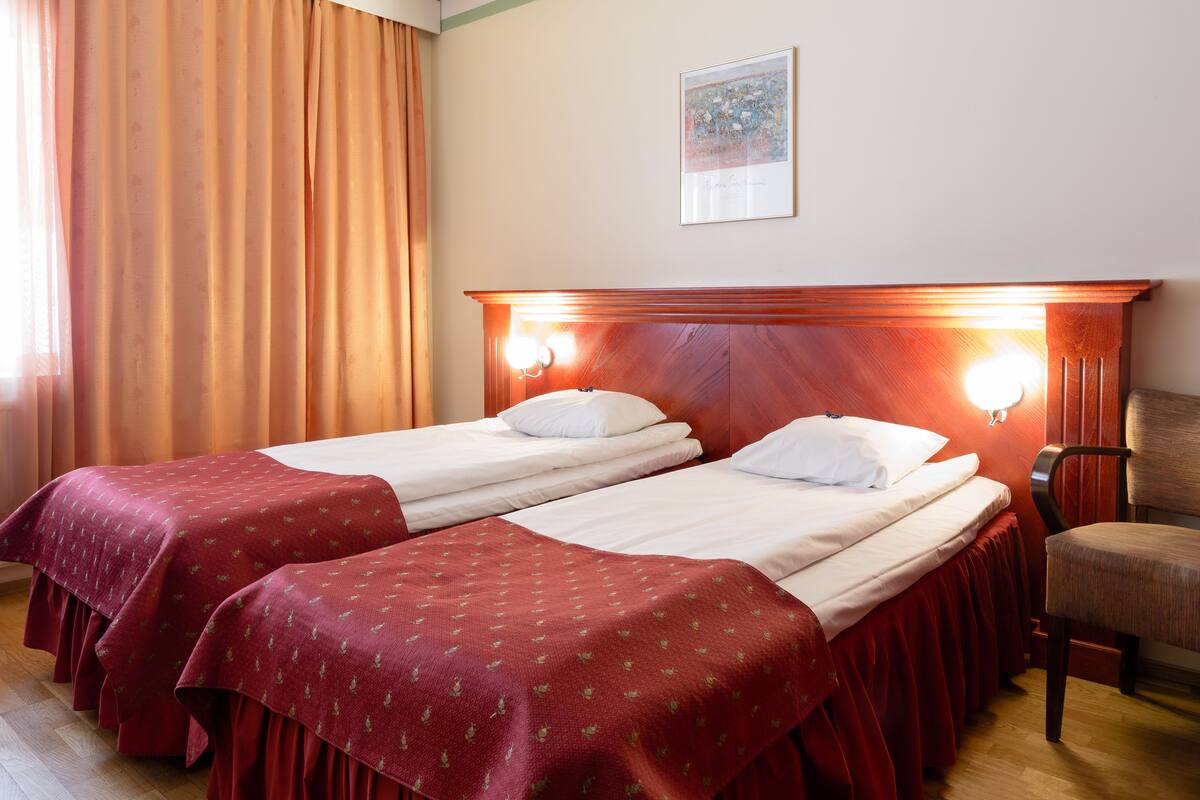 Ein Hotelzimmer mit zwei Einzelbetten, einem Holzkopfteil, einem Sessel und einem Bild an der Wand.