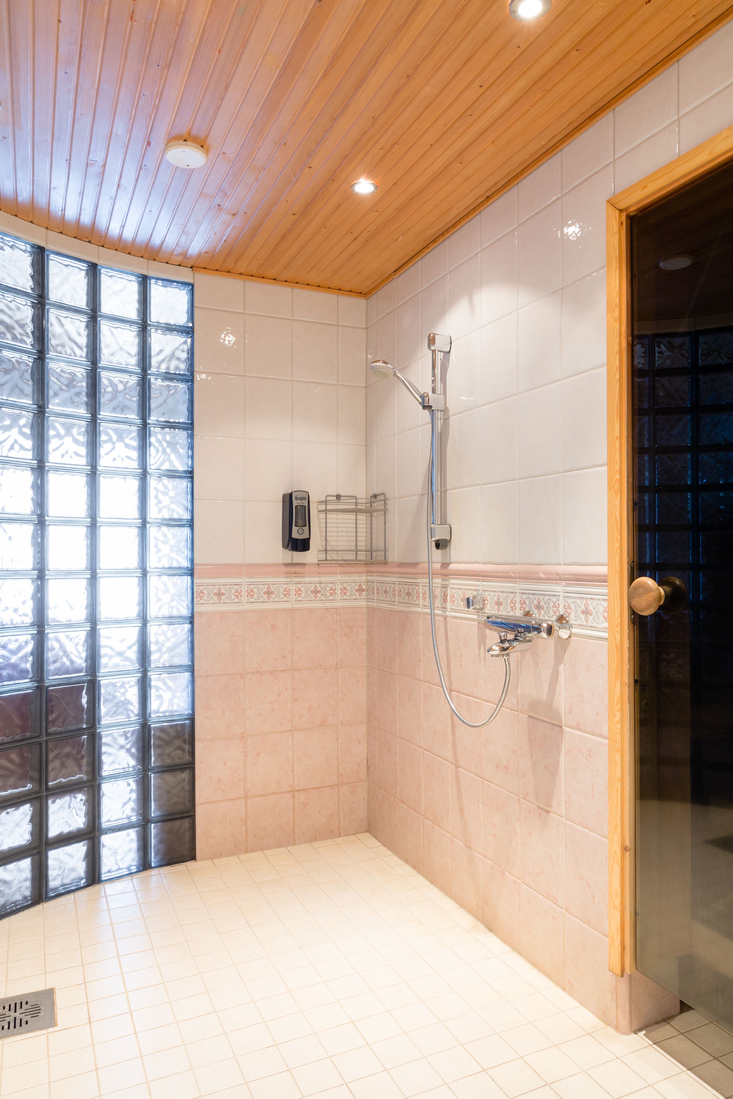 A shower area with a tiled wall, a wooden ceiling, and a glass door.