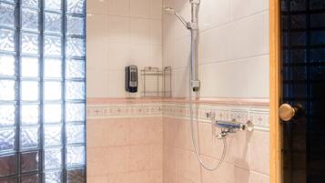 A shower area with a tiled wall, a wooden ceiling, and a glass door.