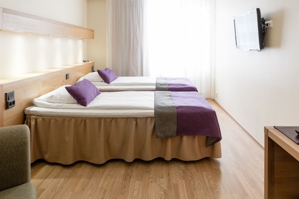 Habitación de hotel con dos camas, cabecero de madera, escritorio y televisor montado en la pared.