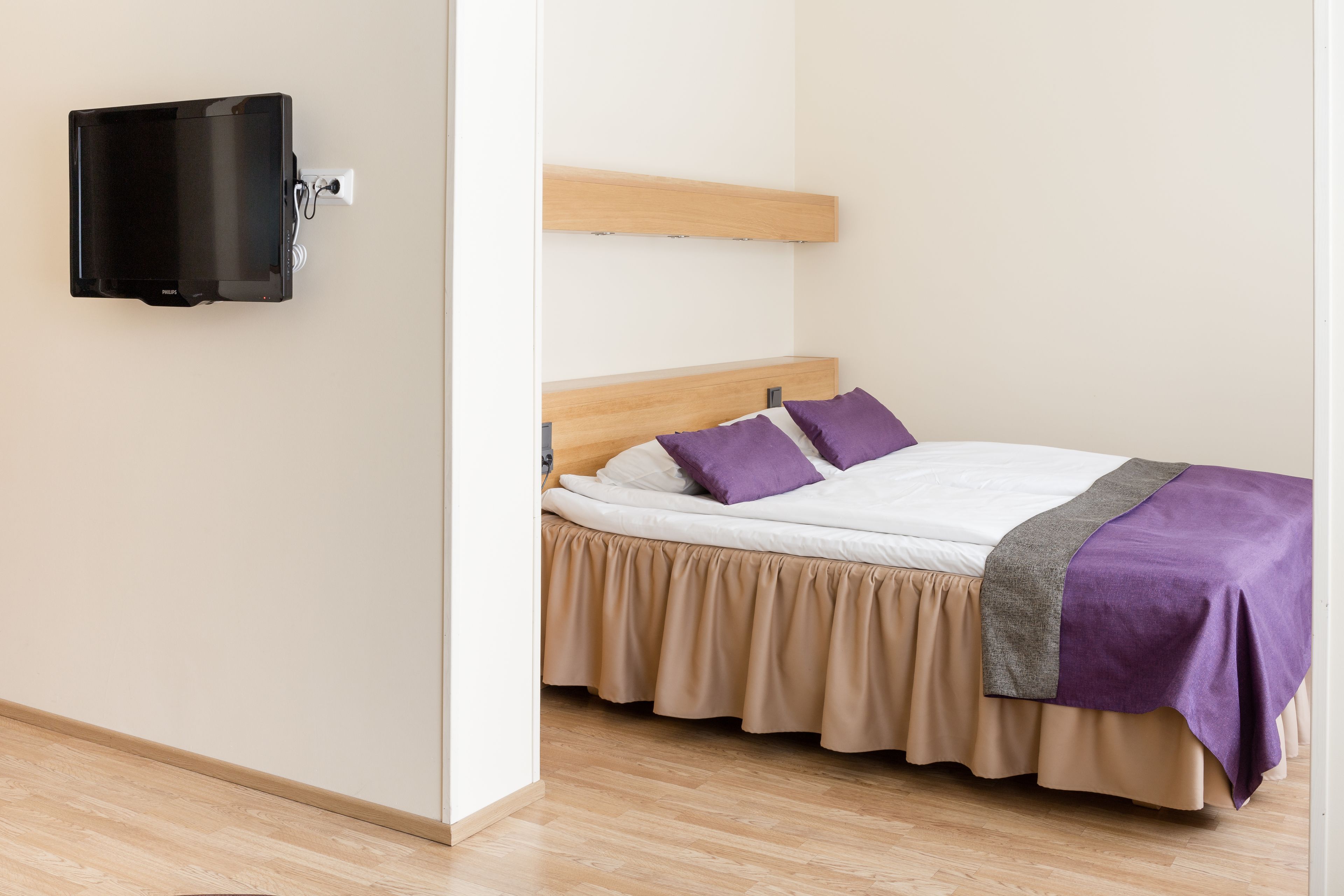 Un dormitorio con cama, televisión montada en la pared y cabecero de madera.