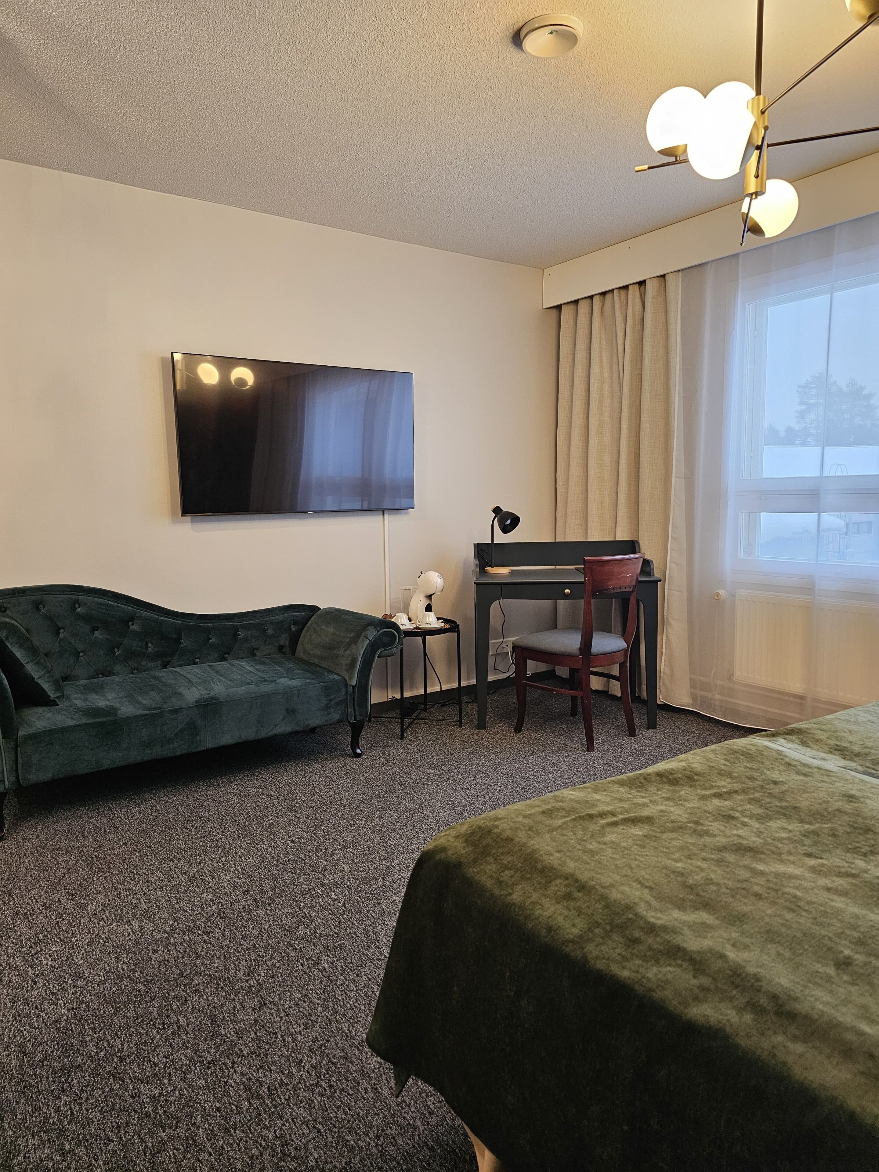 Een hotelkamer met een bank, een bureau met stoel, een televisie en een bed.