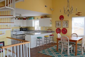 Uma cozinha com armários brancos, uma mesa de jantar com cadeiras, um lustre e uma escada.
