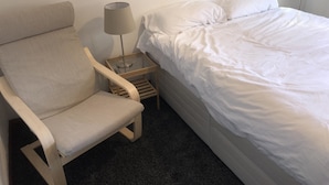 Ett hotellrum med en säng, en stol, ett litet bord med en lampa och ett golv täckt av matta.