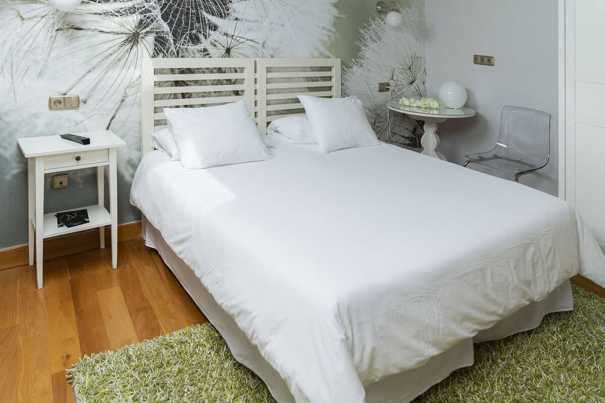 Une chambre bien rangée, avec un lit, une table de chevet et une petite table sur laquelle se trouve une lampe.