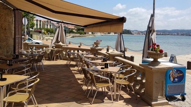 Een terras met tafels en stoelen, een beschaduwd gedeelte en uitzicht op zee.