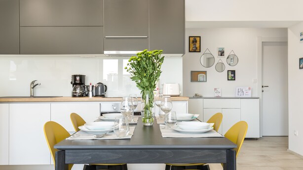A modern kitchen with white cabinets, a dining table set with yellow chairs, and a vase with green flowers. - Lux Private Guest Suite Superb Location (Split)