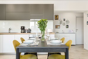 Una cocina moderna con armarios blancos, una mesa de comedor con sillas amarillas y un florero con flores verdes.