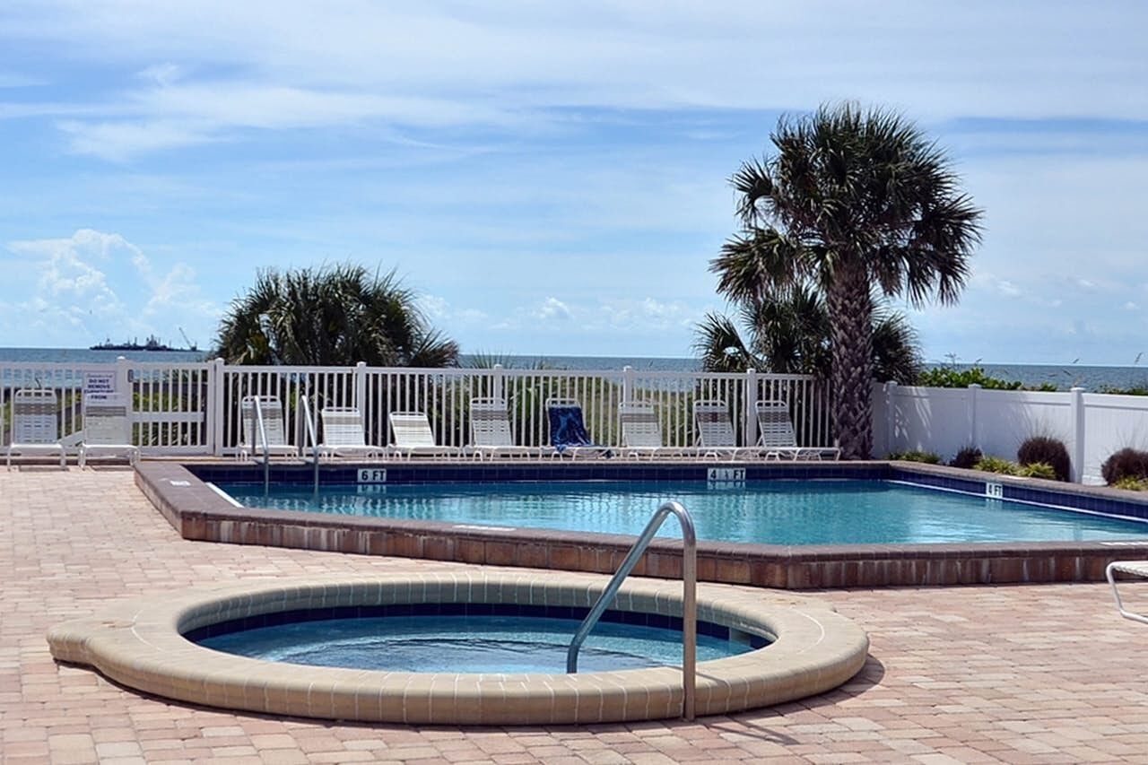 A swimming pool with a hot tub, lounge chairs, and a view of the ocean.