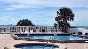 A swimming pool with a hot tub, lounge chairs, and a view of the ocean.