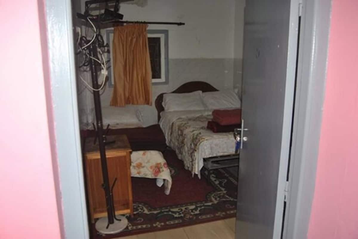 Une petite chambre à coucher, de taille réduite, comprenant un lit simple, une table de chevet, une chaise et une fenêtre avec des rideaux.
