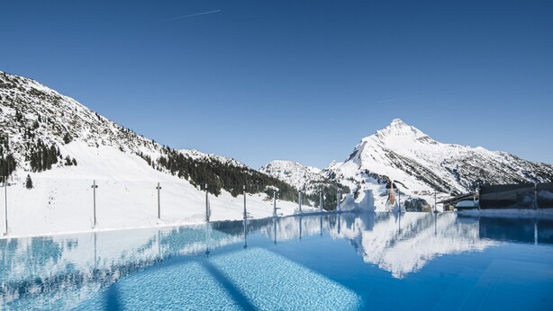 A clear blue pool reflecting a snowy mountain landscape with a clear sky. - AlpenParks Hotel & Apartment Arlberg Warth (Warth)