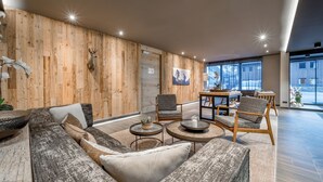 A modern living room with a wooden wall, a sofa, armchairs, a coffee table, and a dining area with a table and chairs. - AlpenParks Hotel & Apartment Arlberg Warth (Warth)