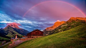 A mountain house with a pool, surrounded by lush green hills and a mountain backdrop. - AlpenParks Hotel & Apartment Arlberg Warth (Warth)