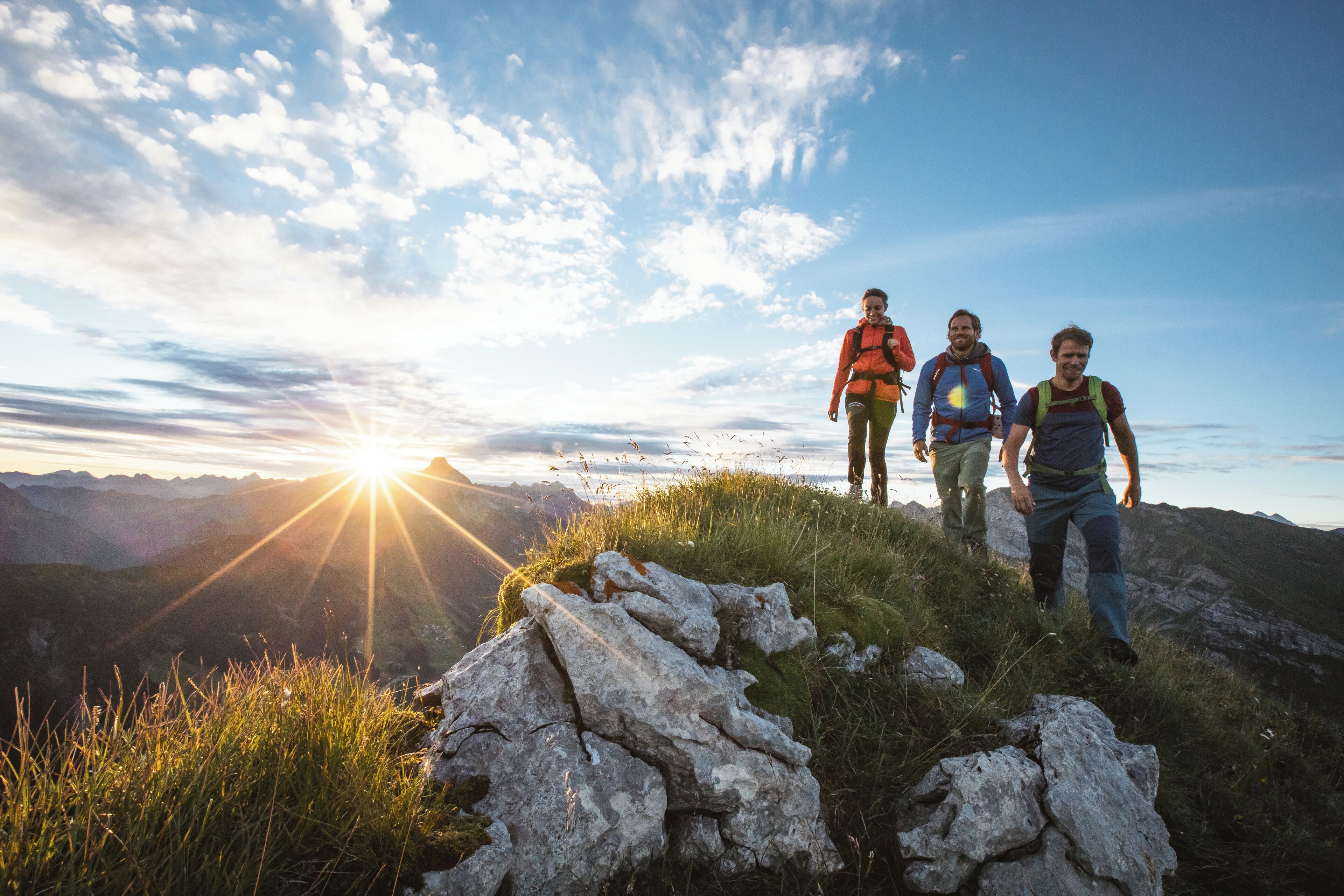 Tres excursionistas en un sendero de montaña al atardecer.