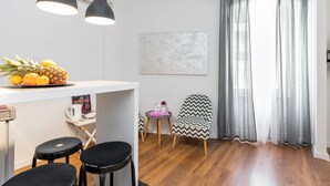 Et moderne køkken med en hvid bordplade, to sorte barstole, en stol med et zigzag-mønster og en skål med ananas og citroner.