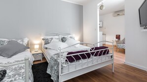 Et moderne soveværelse med en hvid metal seng, et natbord med lampe og et lille skrivebord med stol.