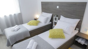 Twee eenpersoonsbedden met witte lakens, een houten hoofdbord, nachtkastjes met lampen en een geel vloerkleed.