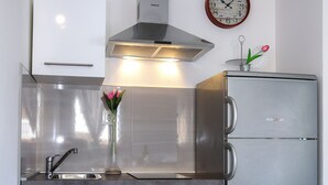 Een moderne keuken met witte kasten, een roestvrijstalen koelkast, een wandklok en een vaas met bloemen.