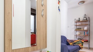 A room with a wooden-framed mirror, a colorful bench, a blue sofa, and a metal shelf with books and decorative items.