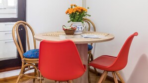 A dining area with a round table, two red chairs, a wicker basket, and a vase with orange flowers.