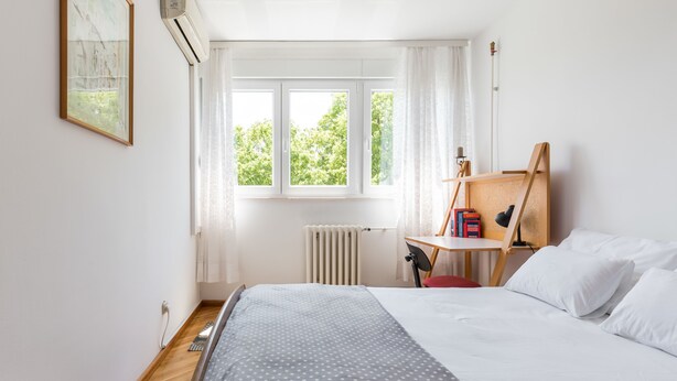 A bedroom with a bed, a desk, a chair, and a window with a view of trees.