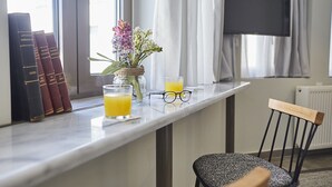 A room with a window, a flat-screen TV mounted on the wall, a bookshelf with books, a vase with flowers, and two glasses of orange juice on a counter. - toStay loft (Athens)