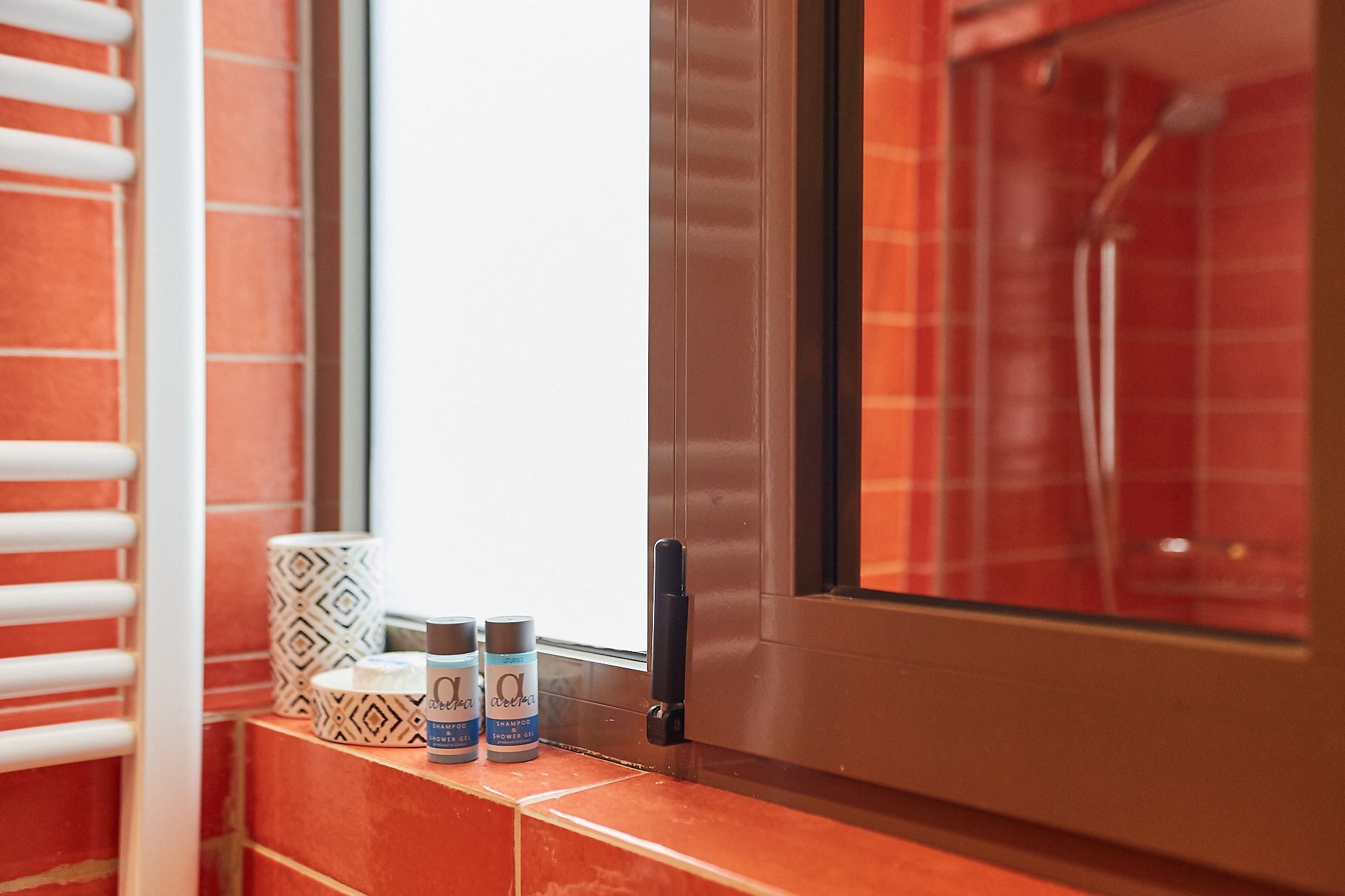 A bathroom with a window, a towel rack, and toiletries on the ledge.