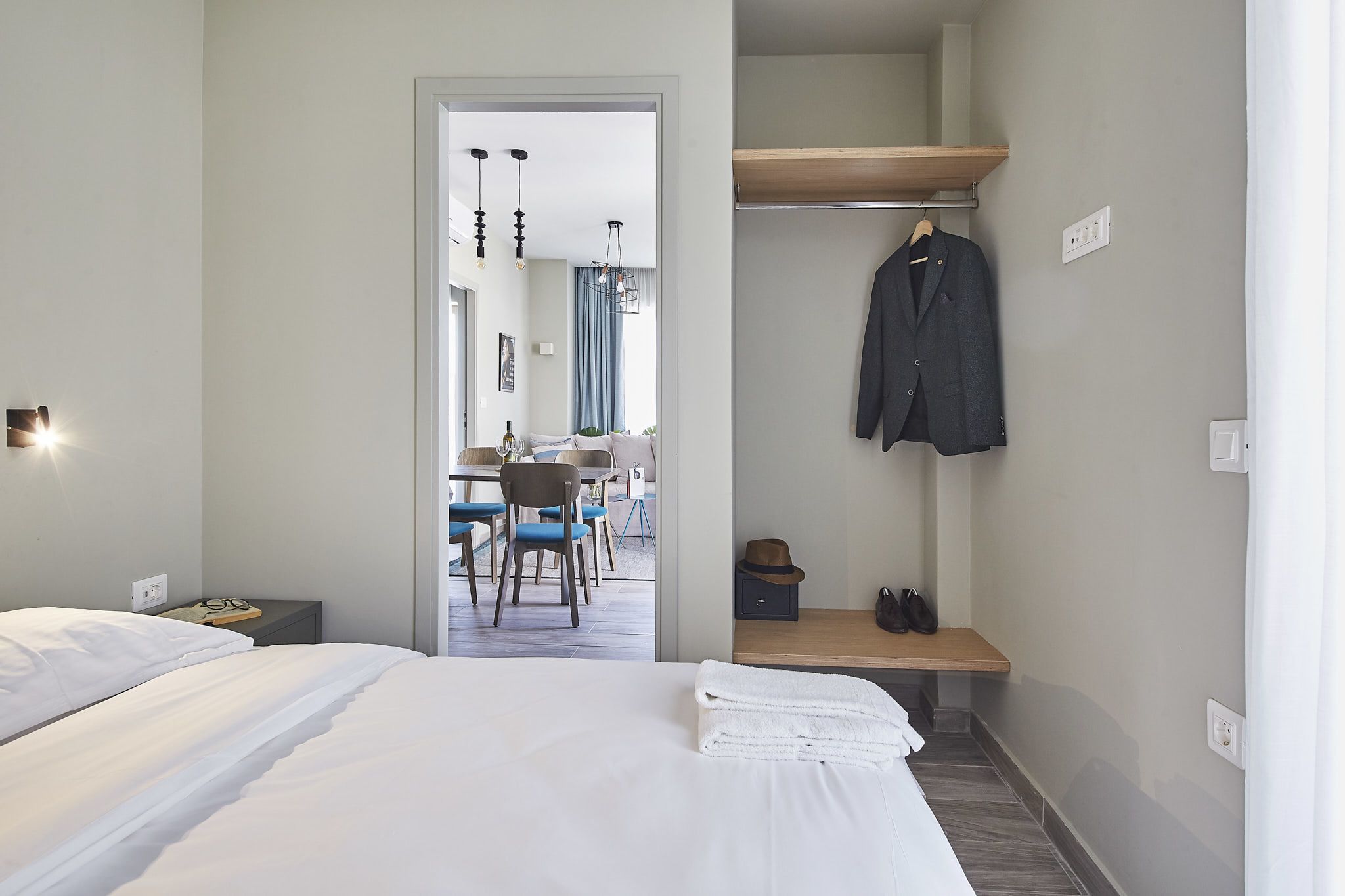 Habitación de hotel con cama, escritorio y silla. Se ve un perchero con una chaqueta y un sombrero.