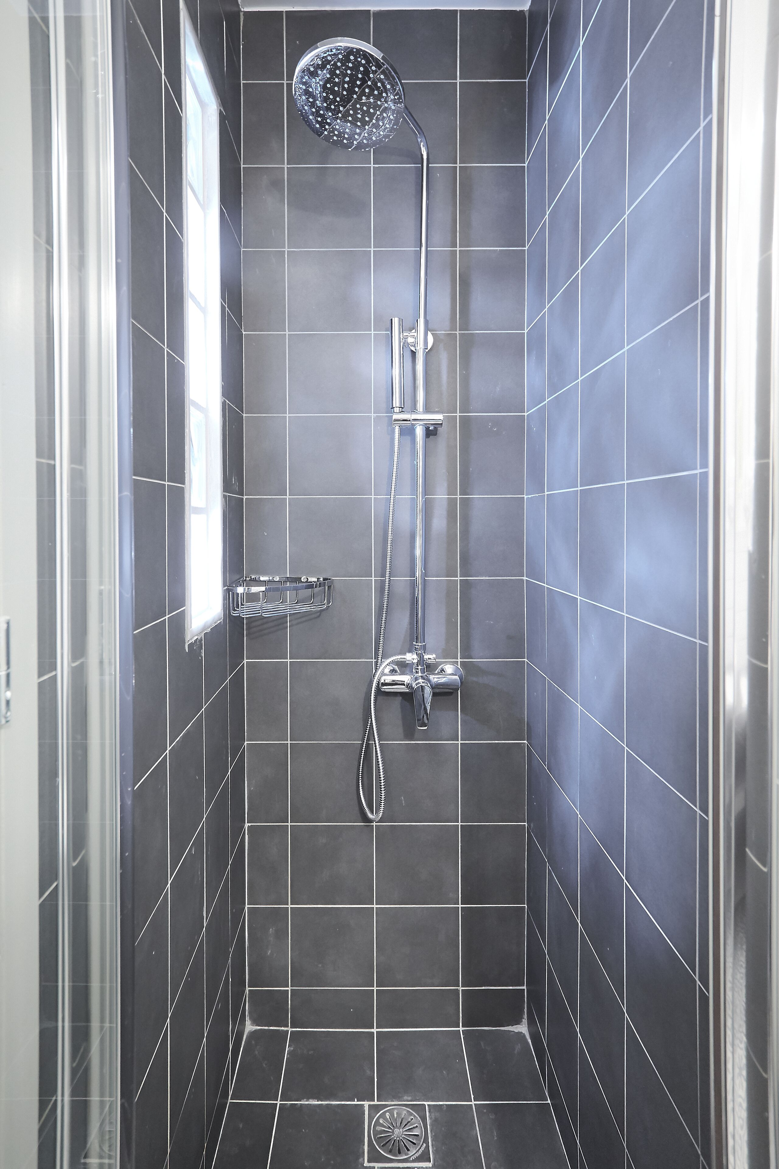 A shower with a handheld showerhead and a wall-mounted faucet.