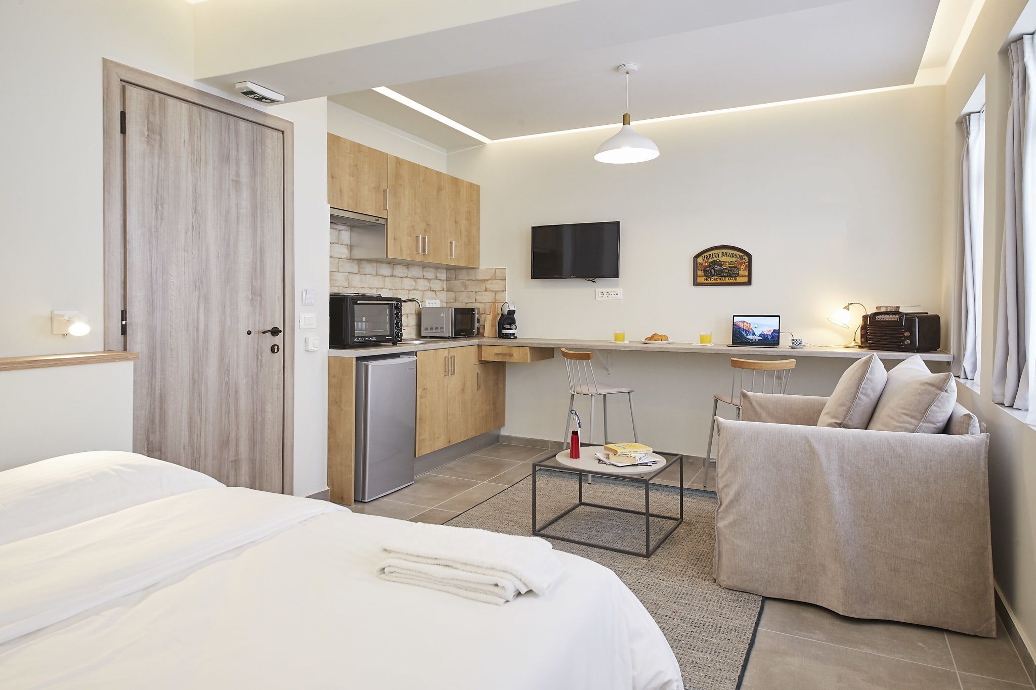 Moderni hotellihuone, jossa on pieni keittiö, televisio ja mukava oleskelualue.