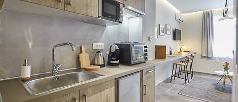 A modern kitchen with wooden cabinets, a stainless steel sink, a microwave, a toaster, and a coffee maker. There is a small refrigerator, a wooden cutting board, and a vase with flowers on the counter.