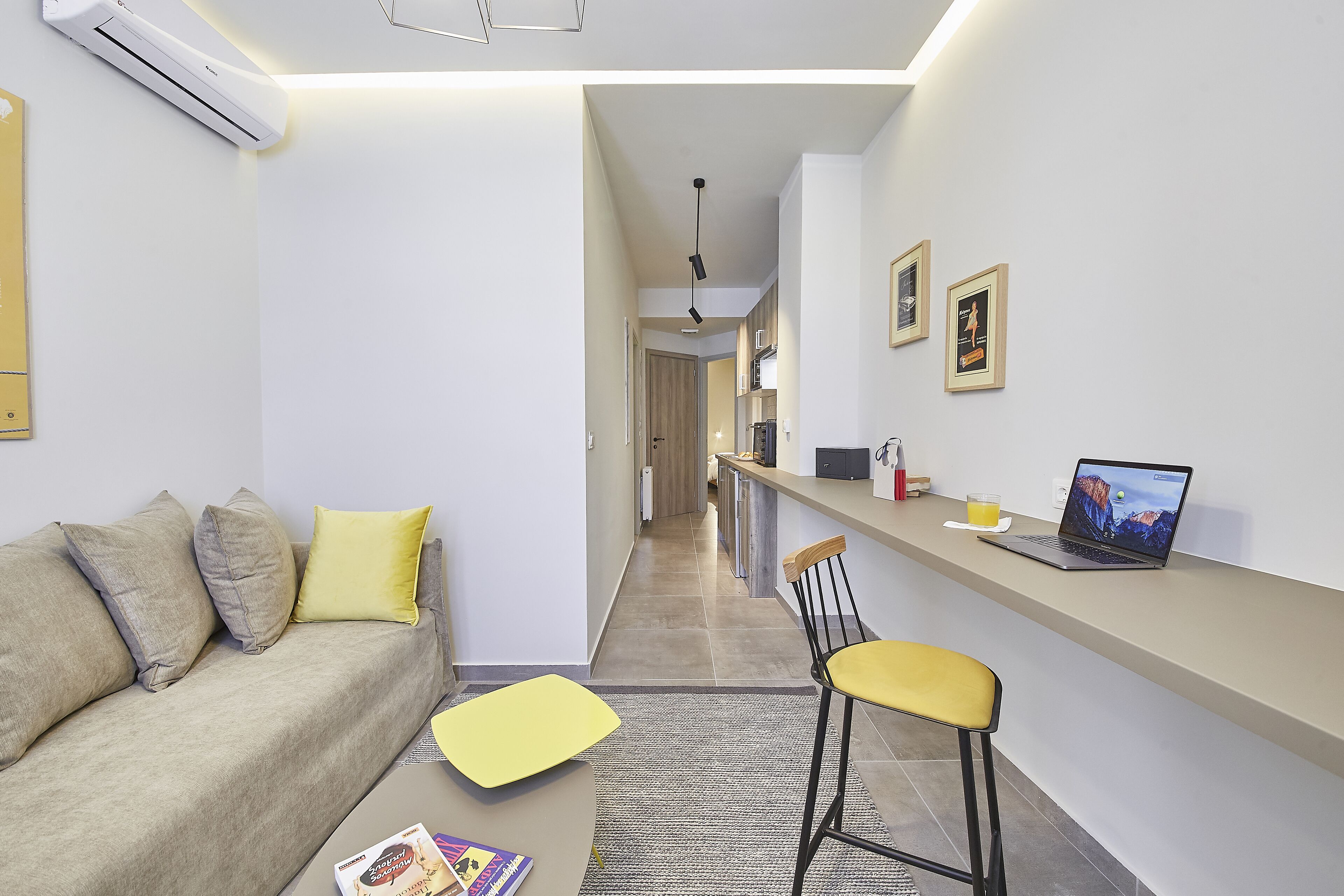 Una sala de estar moderna con un sofá, un reposapiés amarillo, una laptop sobre una encimera y una silla.