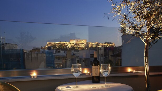 A table with two wine glasses and a bottle, set against a view of a historic building at dusk. - toStay loft (Athens)