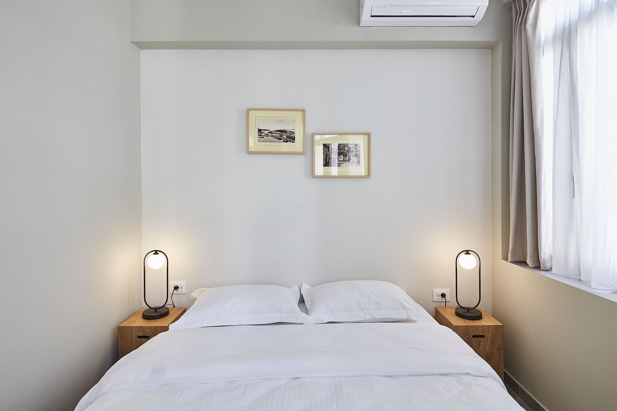 A neatly made bed with white linens, two bedside lamps, and two framed pictures on the wall.