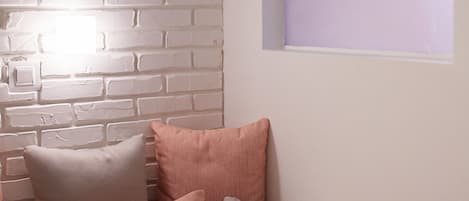 A room with a white brick wall, a window with a purple tint, and a sofa with pink and beige cushions.