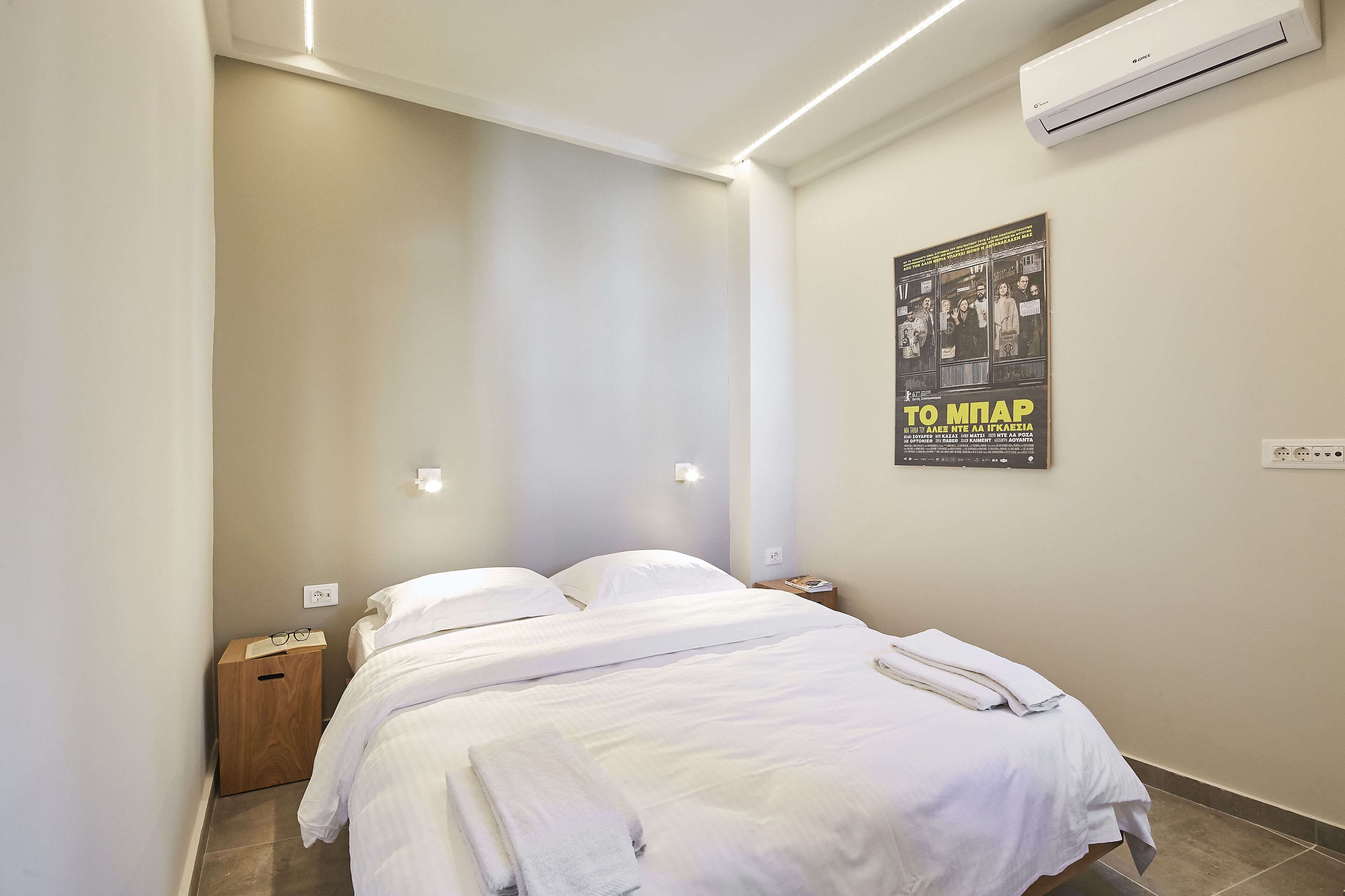 A bedroom with a bed, bedside tables, an air conditioner, and a poster on the wall.