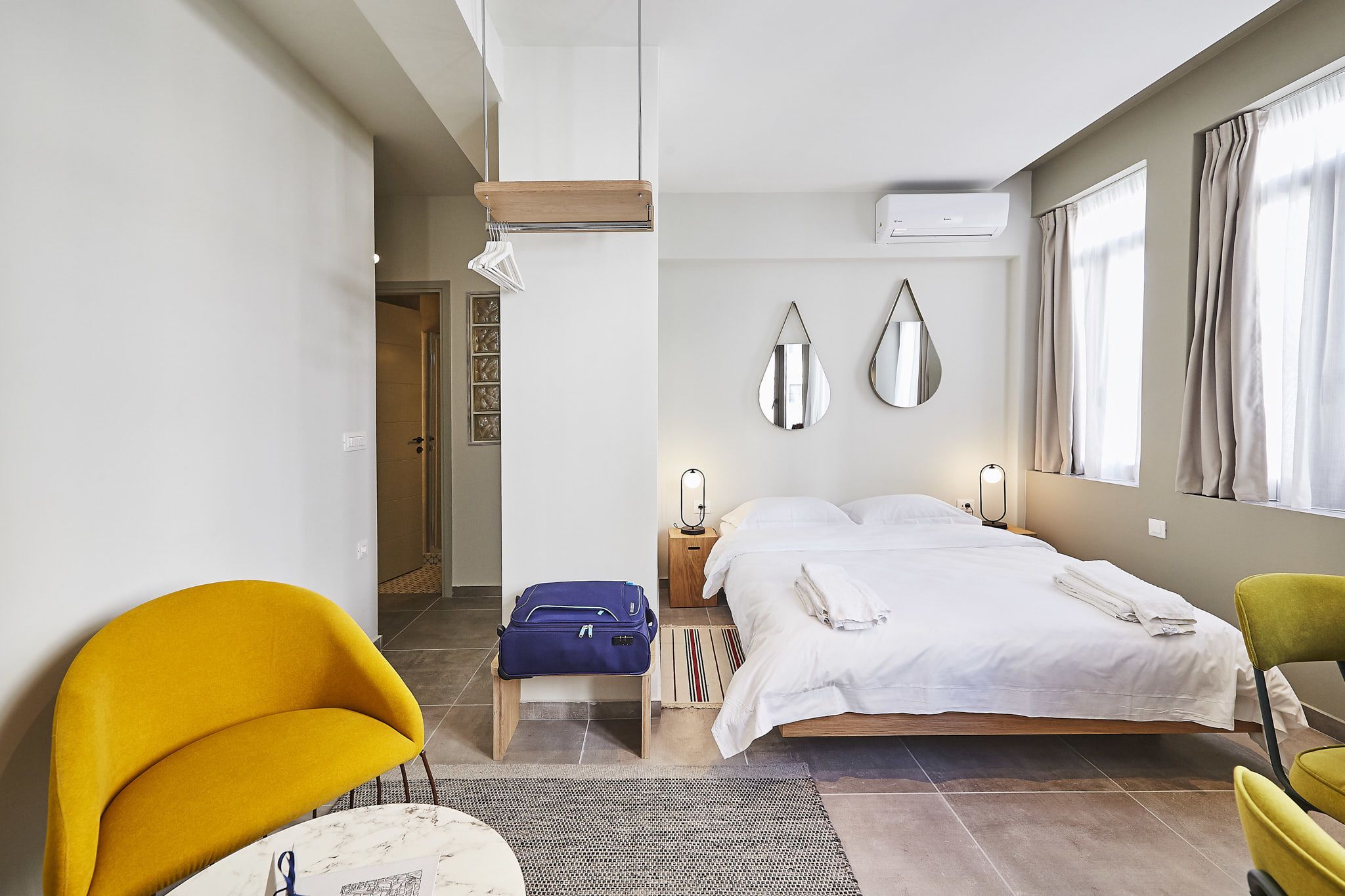 A hotel room with a bed, a desk, a chair, and a suitcase.