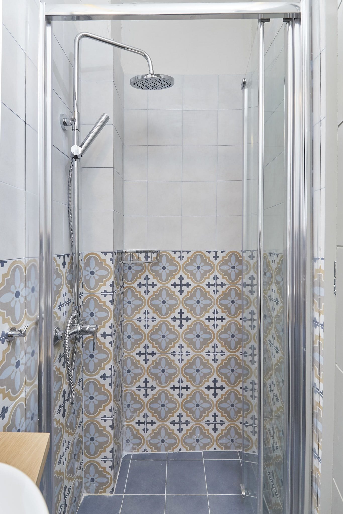 A shower with a glass door, a handheld showerhead, and a wall-mounted faucet. The shower area has patterned tiles.